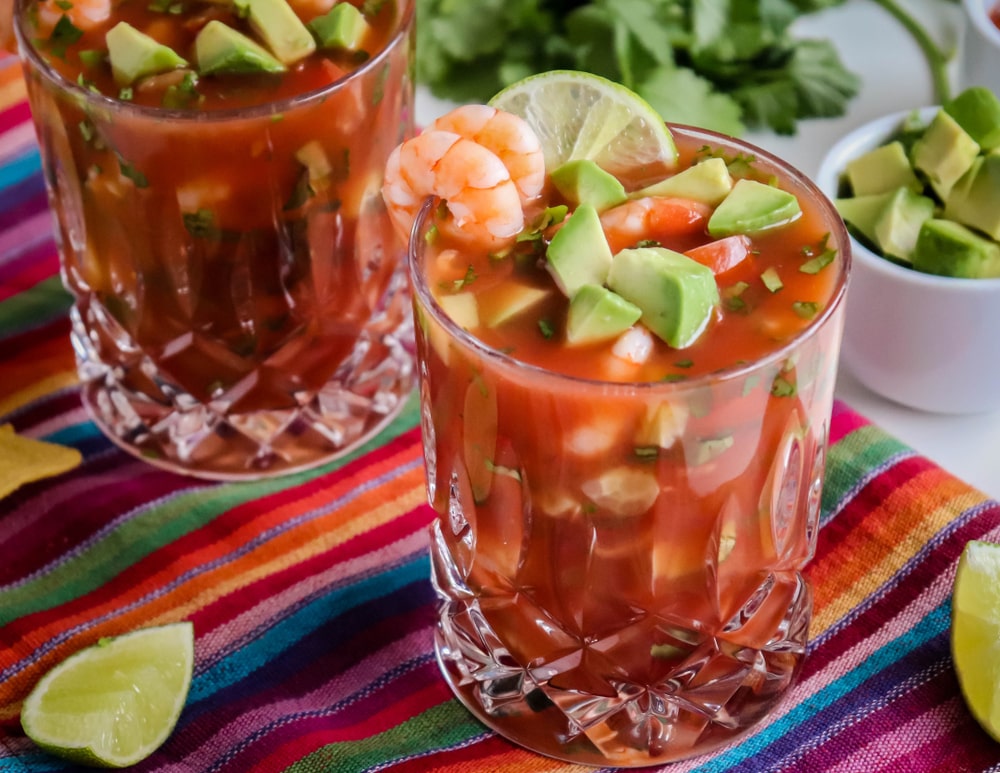 two glasses of mexican shrimp soup with avocado and limes