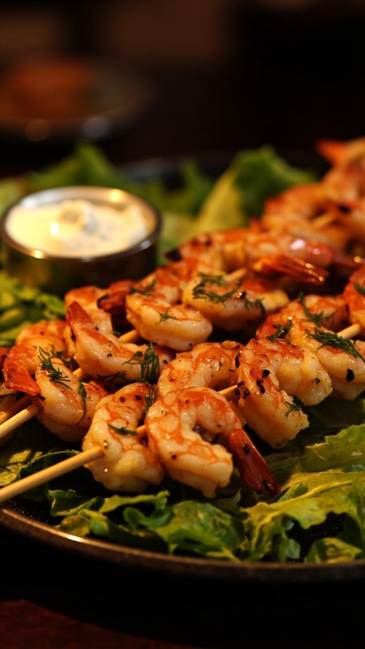 Bamboo skewers threaded with plump shrimp, grilled to a subtle char, sprinkled with minced dill and lemon zest. The skewers are arranged over a bed of lettuce on a platter, with a bowl of yogurt-dill sauce at the side.