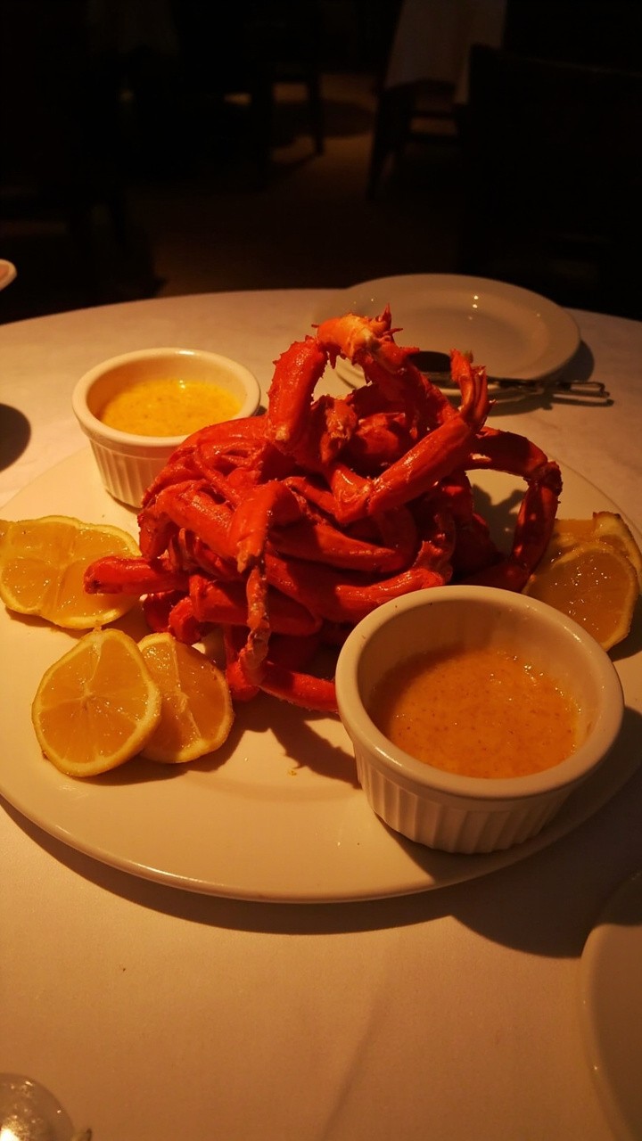 A pile of bright red king crab legs stacked on a round white platter, with two small bowls of golden drawn butter and lemon wedges along the side. A pile of bright red king crab legs stacked on a round white platter, with two small bowls of golden drawn butter and lemon wedges along the side.