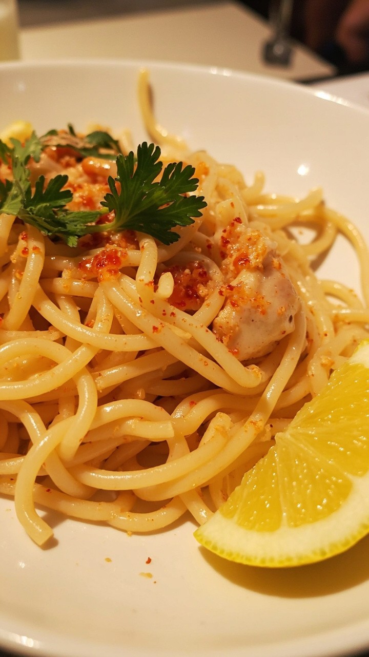 Twirled spaghetti coated in a glossy, lemony sauce with visible chunks of crab meat, finished with red pepper flakes and parsley in a shallow white bowl, lemon wedges on the side. Twirled spaghetti coated in a glossy, lemony sauce with visible chunks of crab meat, finished with red pepper flakes and parsley in a shallow white bowl, lemon wedges on the side.