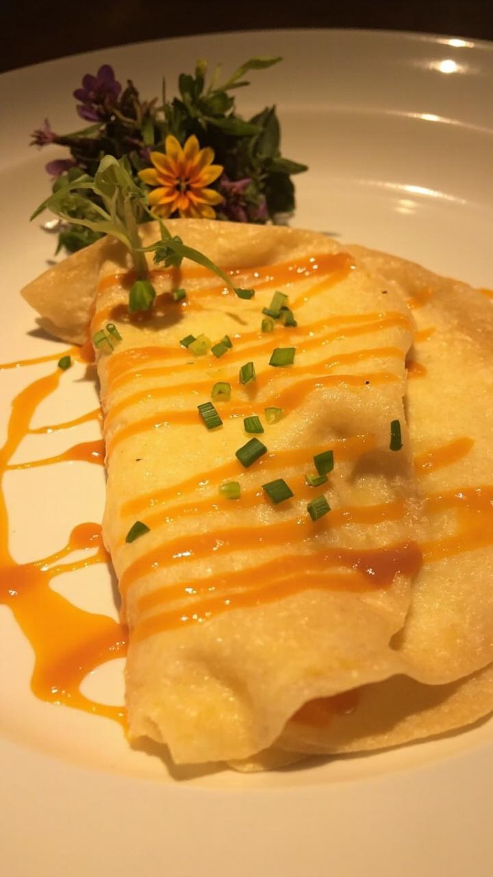 Thin golden crepes folded over creamy lobster Newburg filling on a white plate topped with chopped chives and a small mixed herb garnish with a drizzle of sauce on the plate