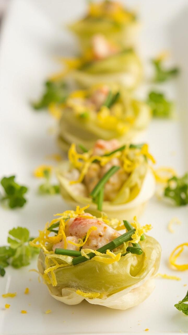 Crisp endive leaves filled with creamy lobster Newburg garnished with chopped chives and thin lemon zest strips arranged on a white platter with scattered microgreens