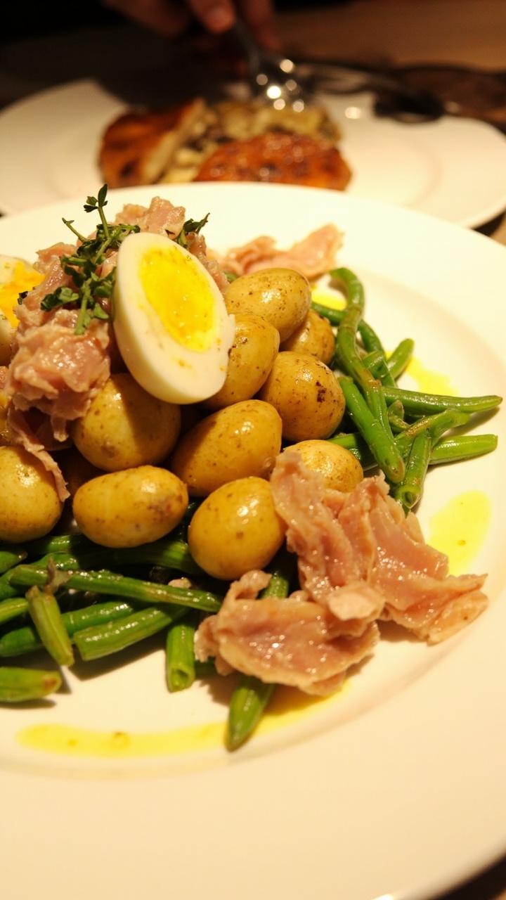 Plate with a neat pile of baby potatoes, green beans, flaked tuna, halved hard-boiled egg, a drizzle of vinaigrette and a sprinkle of parsley