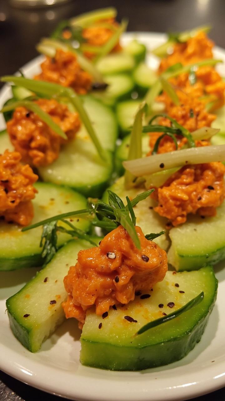 Thick slices of cucumber topped with a dollop of spicy crab filling, sprinkled with sesame seeds and sliced green onions, arranged on a round serving tray.