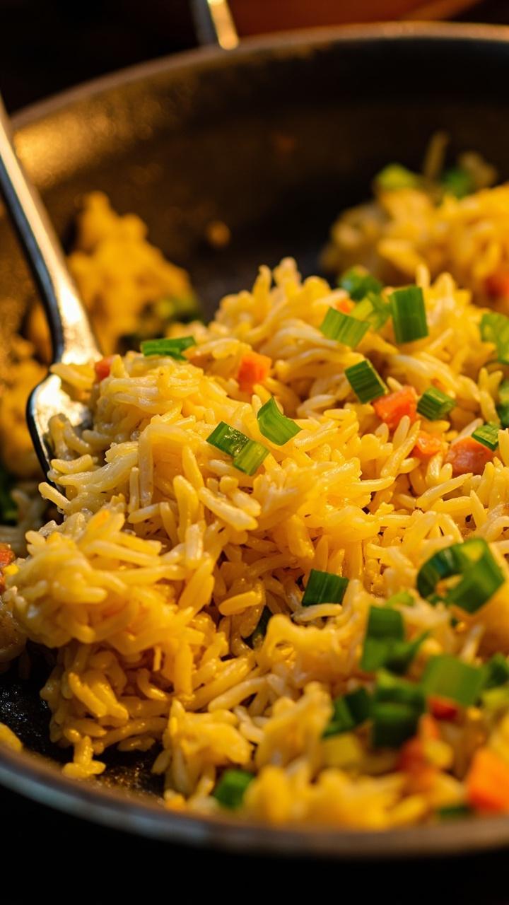 Golden flecks of scrambled egg mixed with separated long rice grains, bright green scallion rounds, small bits of carrot and peas, presented in a shallow black skillet with serving spatula. Golden flecks of scrambled egg mixed with separated long rice grains, bright green scallion rounds, small bits of carrot and peas, presented in a shallow black skillet with serving spatula.